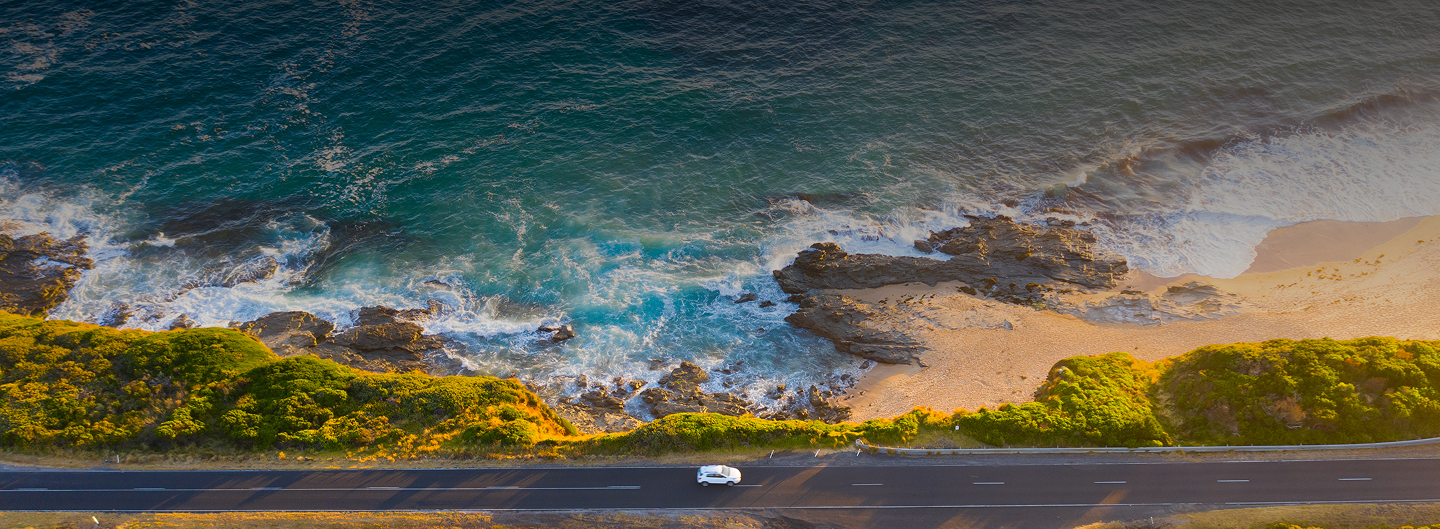 A aerial, top-down view of a coastal highway with waves crashing against the shore.