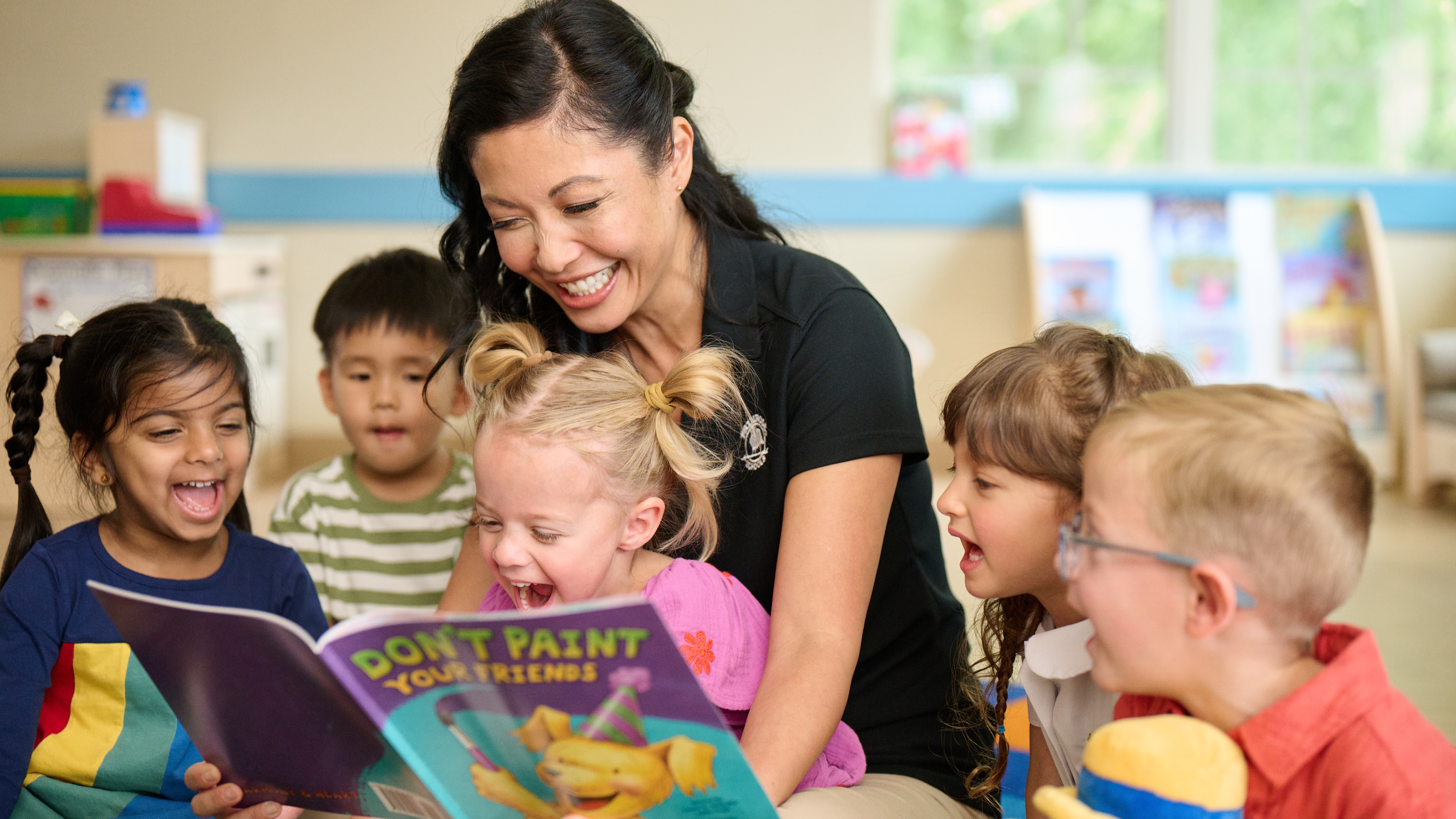 Primrose Schools teacher reading Don't Paint Your Friends picture book to diverse group of laughing preschoolers