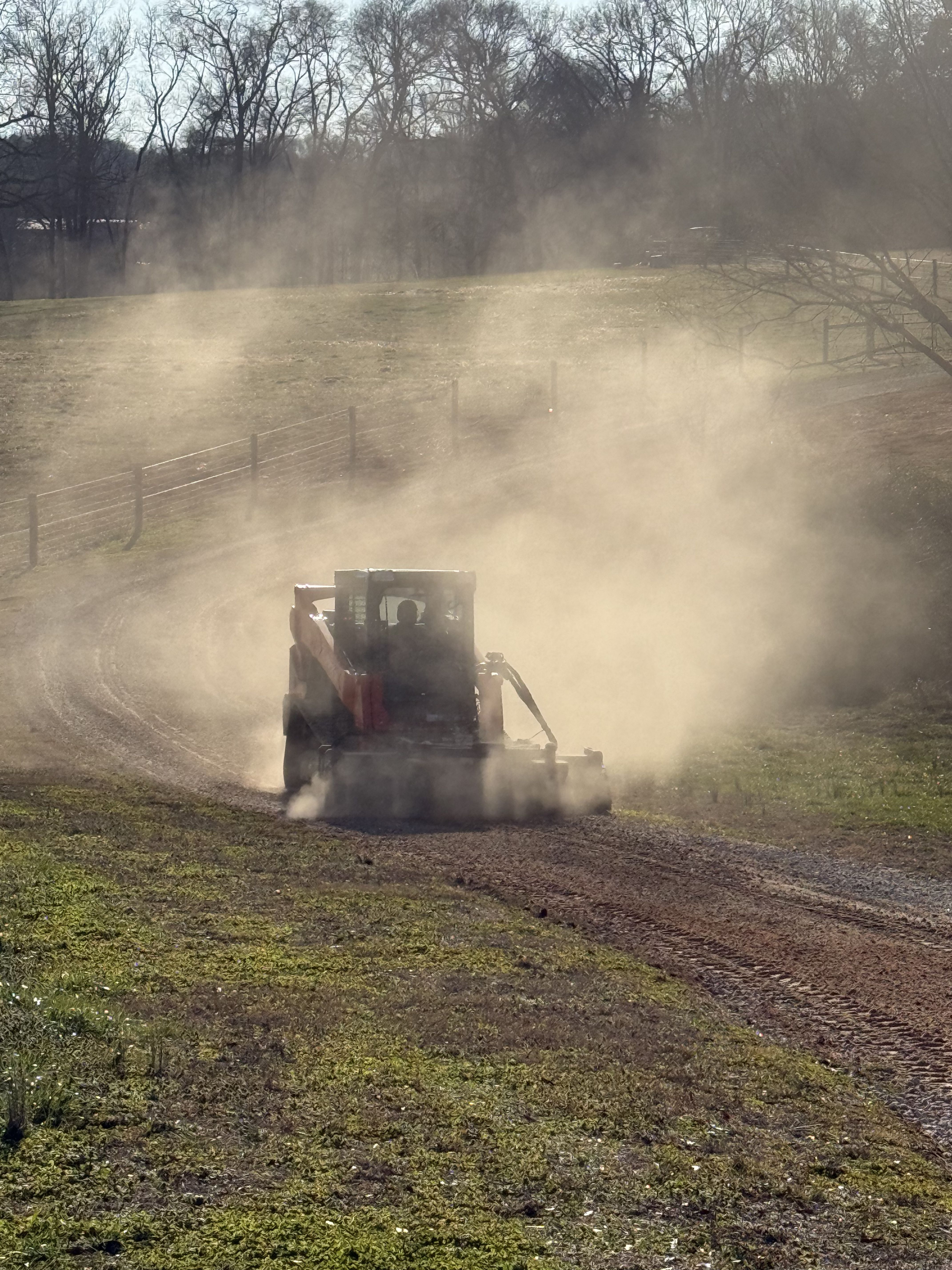 Photo of heavy equipment working through a dusty property area during land clearing, grading, or driveway/site preparation services.