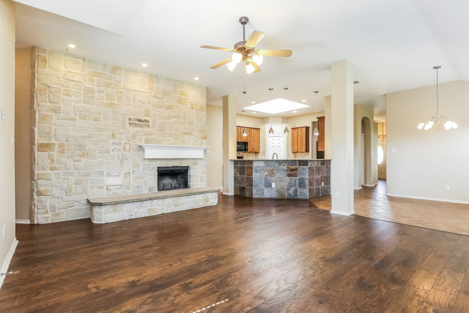Family room with a large stone fireplace connected to a kitchen with a bar at Invitation Homes Dallas.