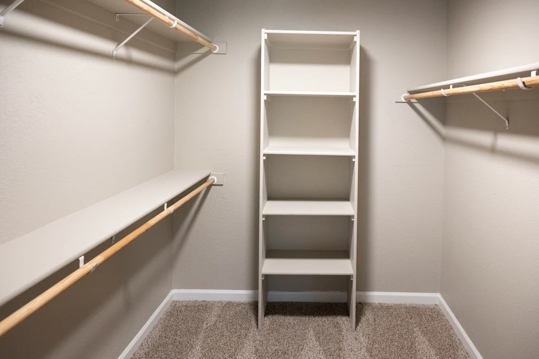 A room with a carpeted floor and a white wall with a shelf and a rack