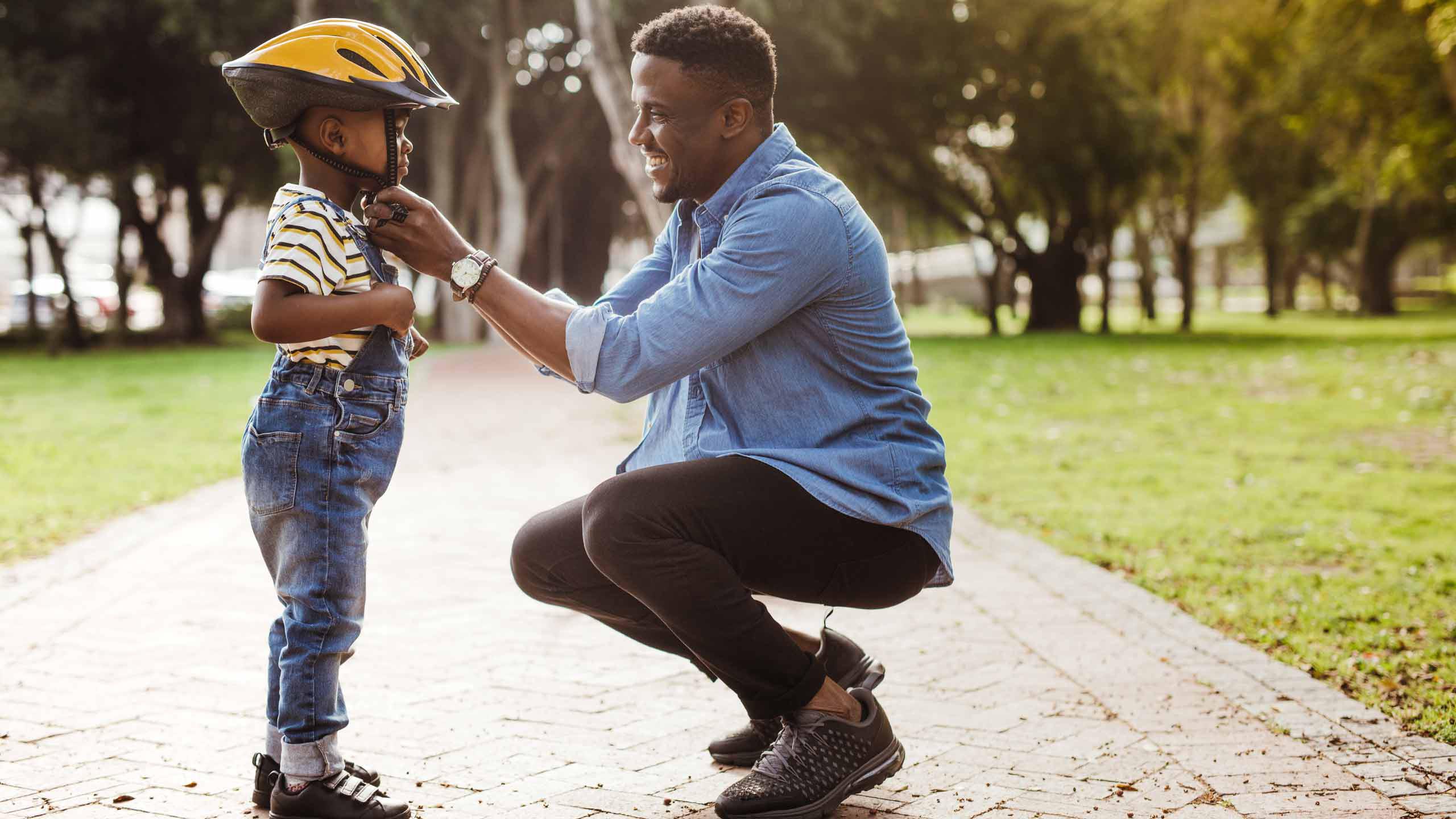 A father fastening a helmet for his son in a park