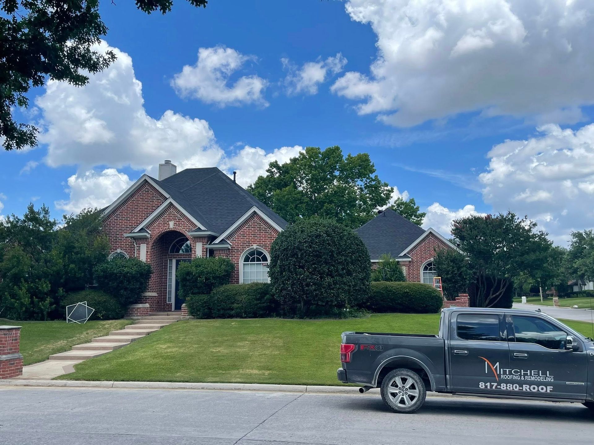 Completed roofing project featuring a large brick home with a new dark shingle roof, manicured lands 