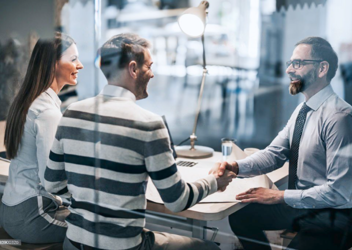 An advisor shaking hands with a client couple.