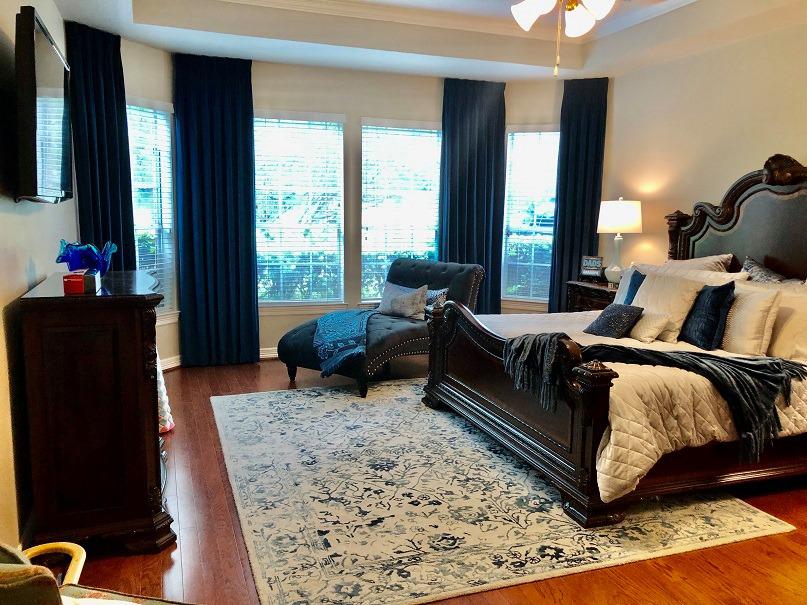 This Richmond, TX master bedroom combined Floating Drapery Panels with Faux Wood Blinds to create the ultimate masterpiece with window treatments! The style is out of this world beautiful. #BudgetBlindsKatySugarLand #FreeConsultation #DraperyPanels #FauxWoodBlinds