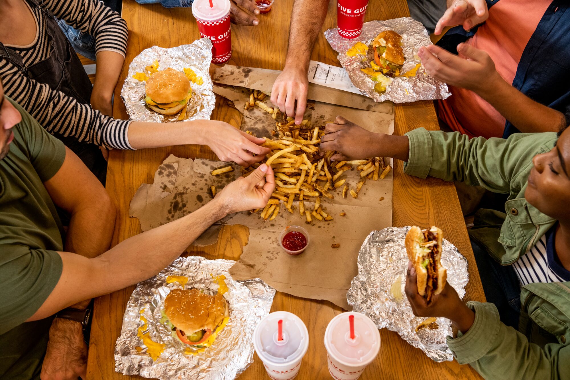 A top-down photograph of a group of friends sharing an order of fries alongside their sandwiches at  Five Guys Thousand Oaks (805)496-0173