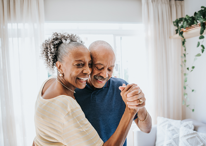 An elderly couple dancing together in their living room.