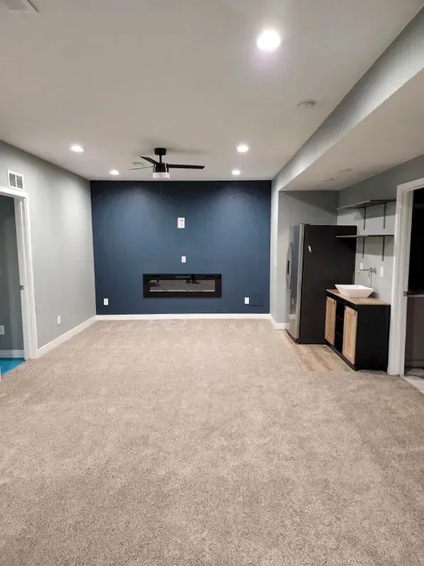 Stylish basement entertainment room featuring plush carpeting, recessed lighting, accent wall, fireplace, ceiling fan, and wet bar, designed for relaxation, movie nights, and social gatherings.