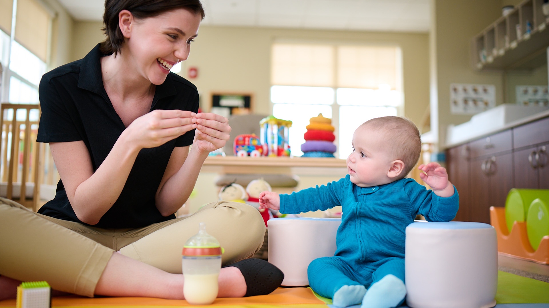 Primrose Schools infant teacher doing interactive play with baby on colorful floor mat in childcare classroom