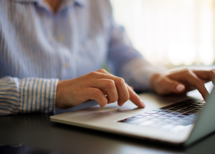 Close-up of a professional in a striped shirt typing on laptop at desk.