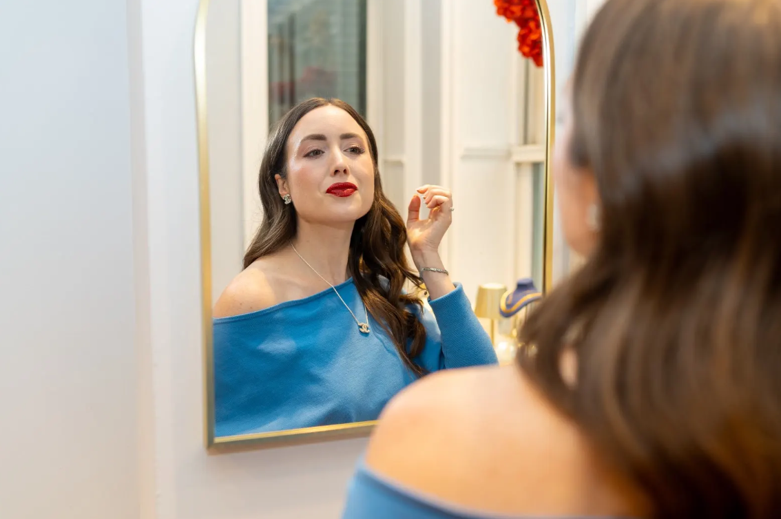 A mirror captures a blue off-shoulder look styled with a pendant necklace, earrings, and a bracelet at Eliana Curated in Old Town Alexandria, VA. Discover jewelry that adds elegance to everyday style.