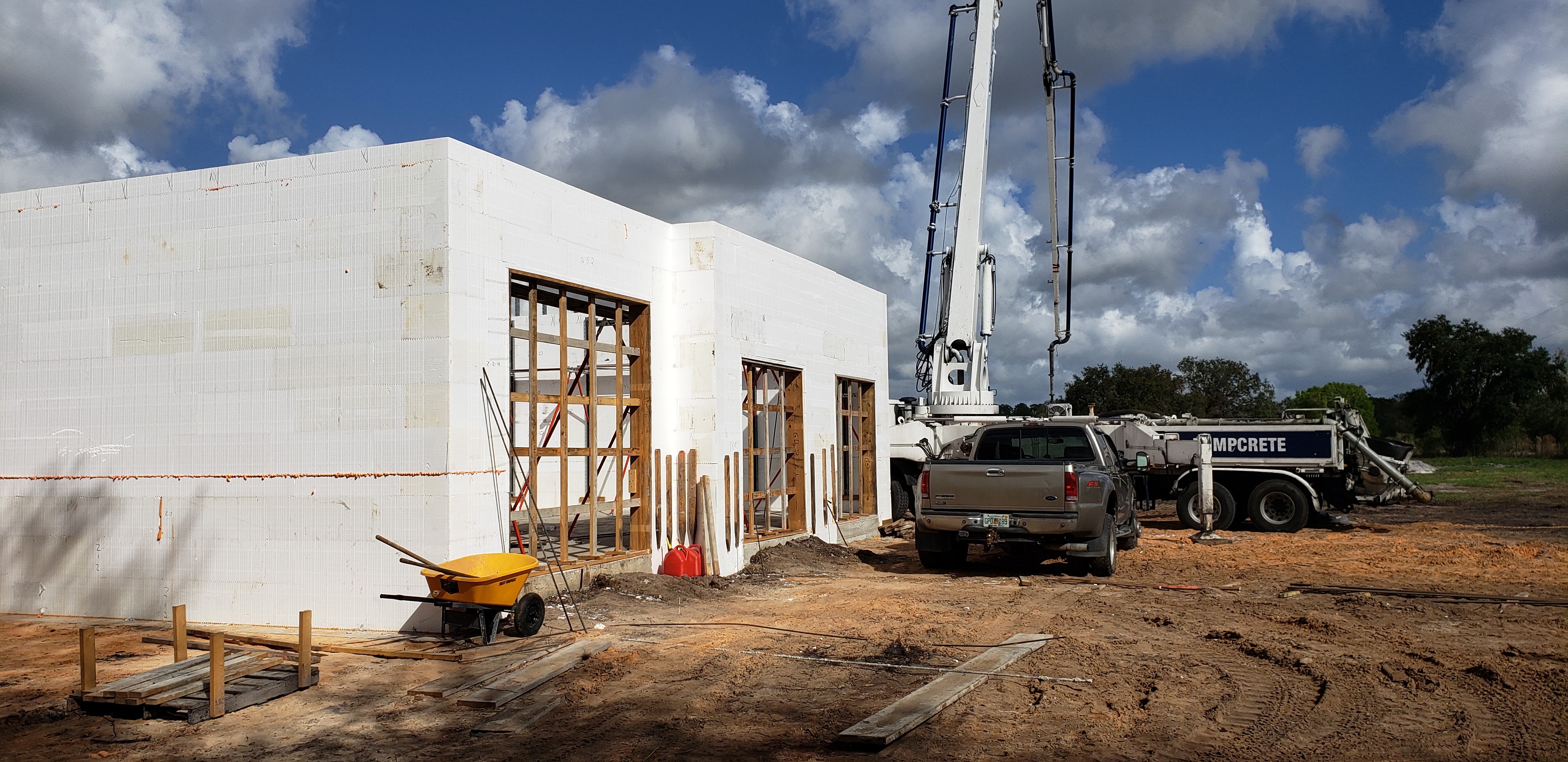 A construction site with a building under construction, a concrete pump truck, and a pickup truck pa 