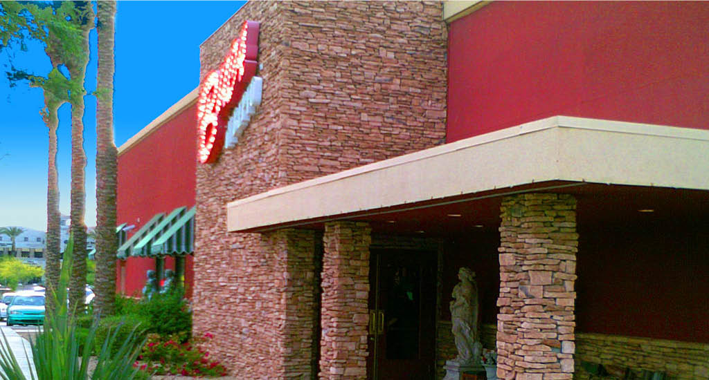 Closeup exterior of Buca di Beppo Mesa with a Buca sign lit up on brick accent.