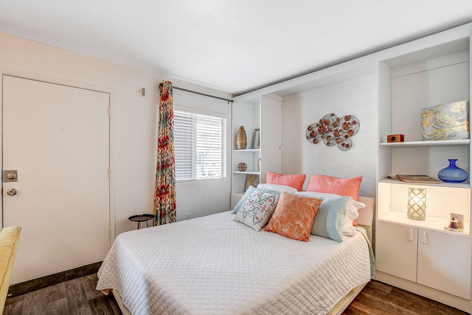 A bedroom with a bed, a window with a curtain, and a wall art