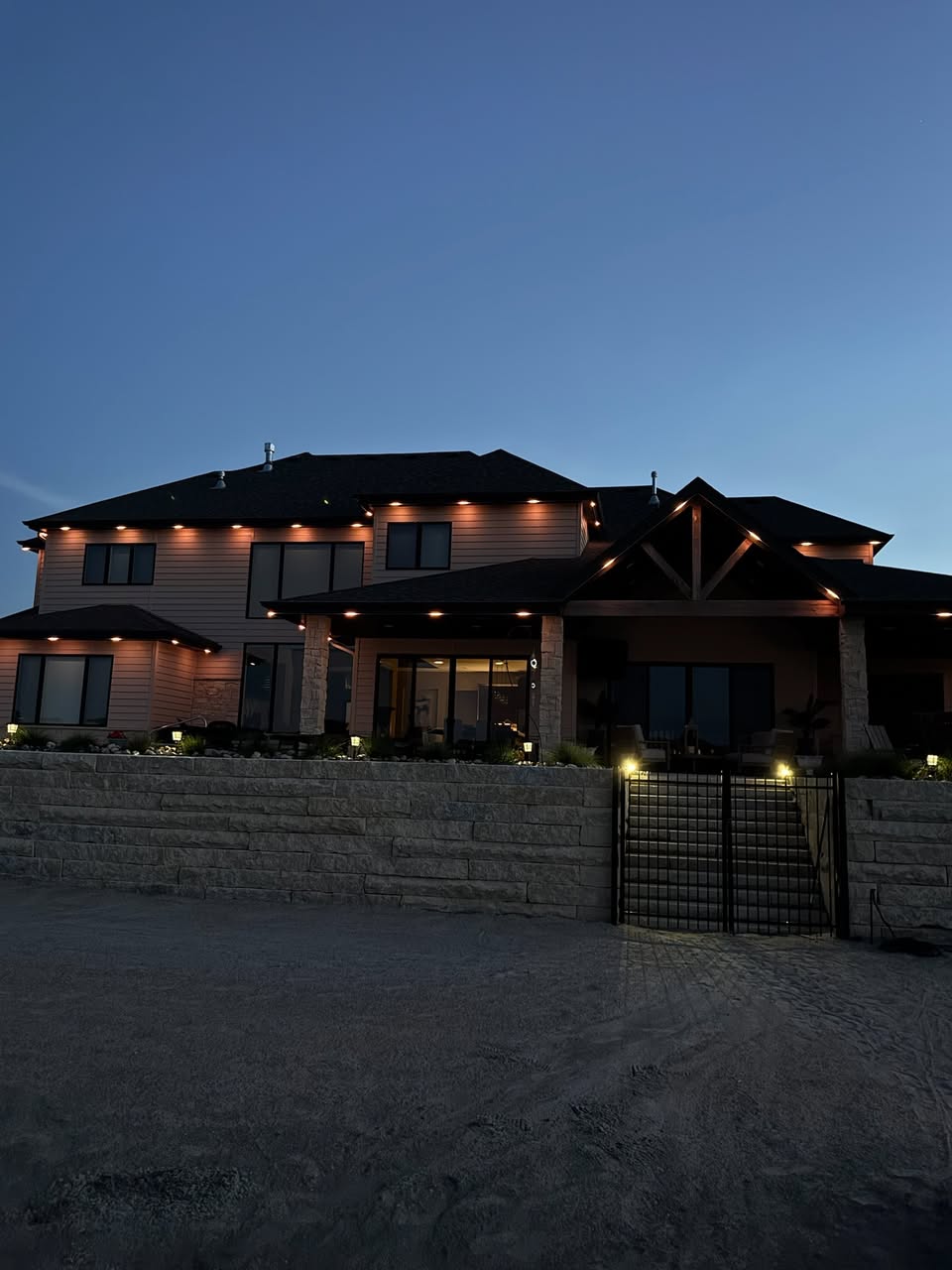 Warm exterior accent lighting illuminating the roofline and architectural details of a large residential property at dusk.