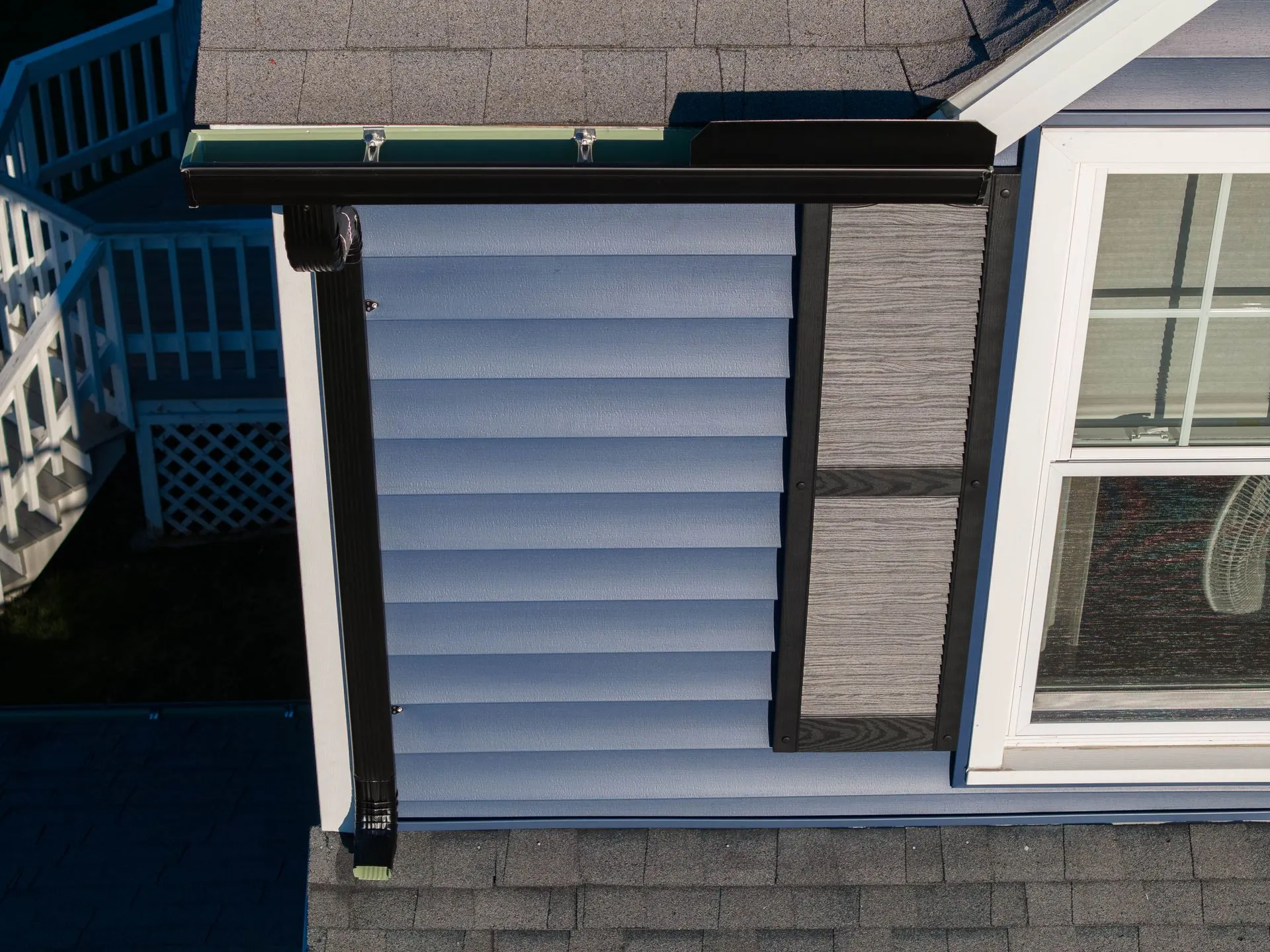 Modern black gutter system installed on a home exterior with contrasting siding. Stylish design comb 