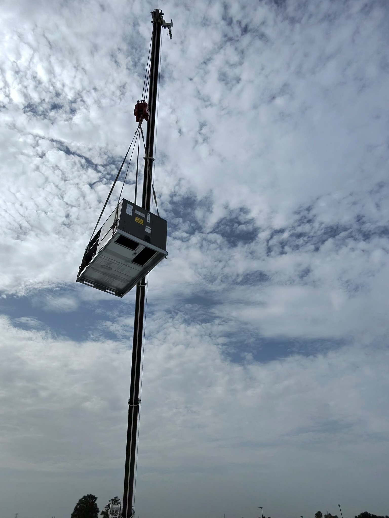 Rooftop air conditioning unit suspended from a crane during a professional commercial HVAC replaceme 