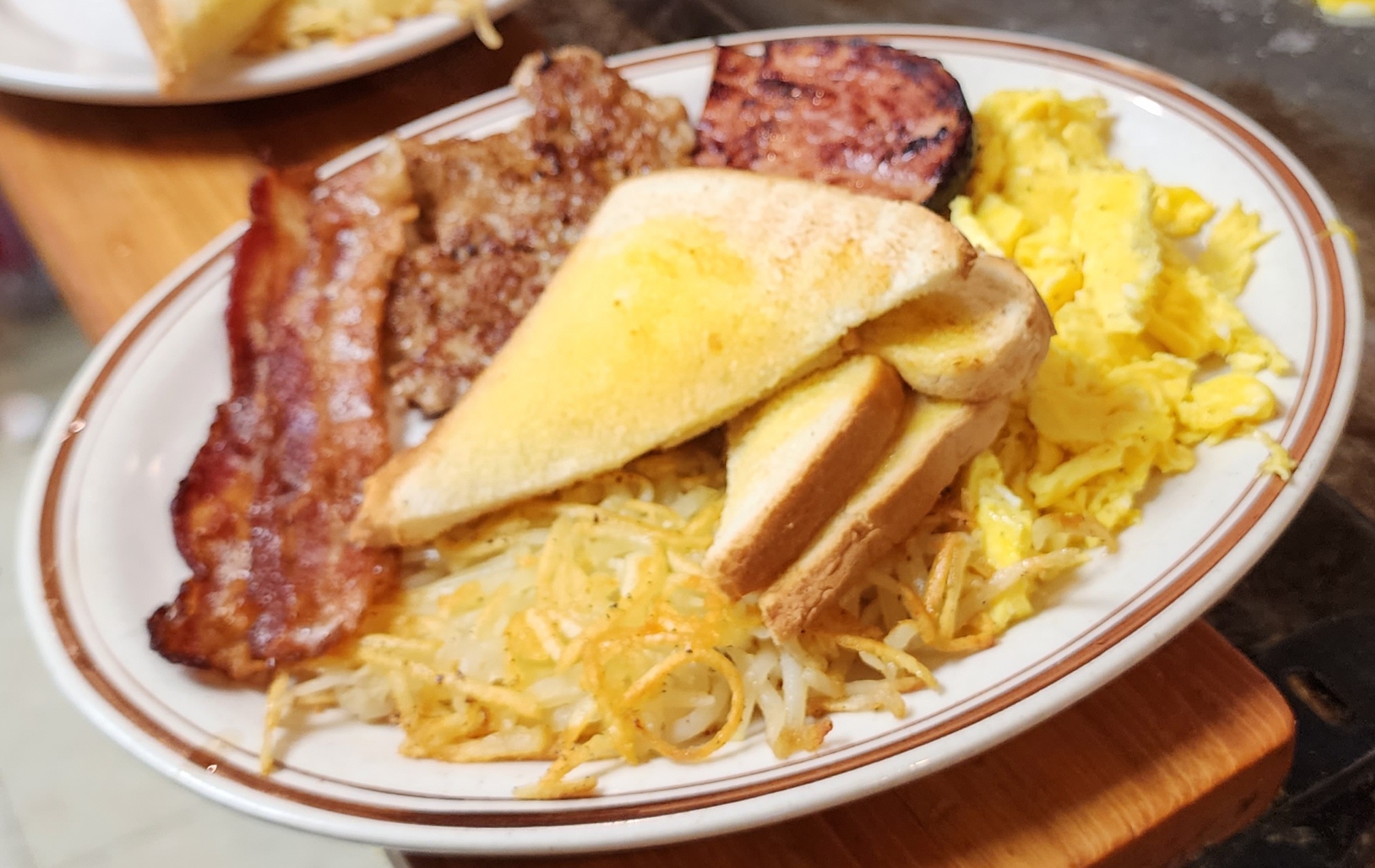 A breakfast platter with eggs, bacon, sausage, ham, hashbrowns, and toast.