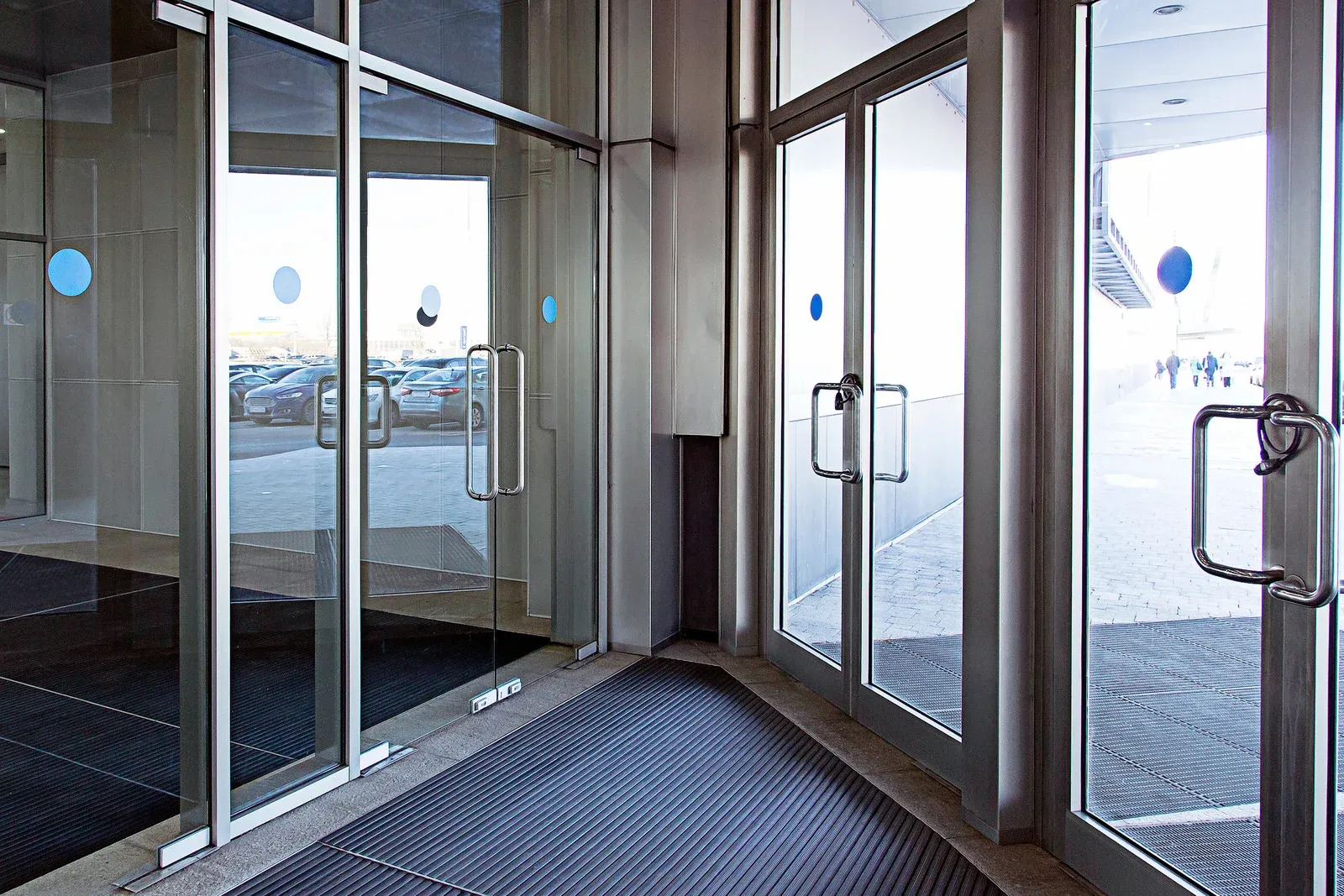 Modern commercial entrance features multiple full-height glass doors with metal frames, pull handles 
