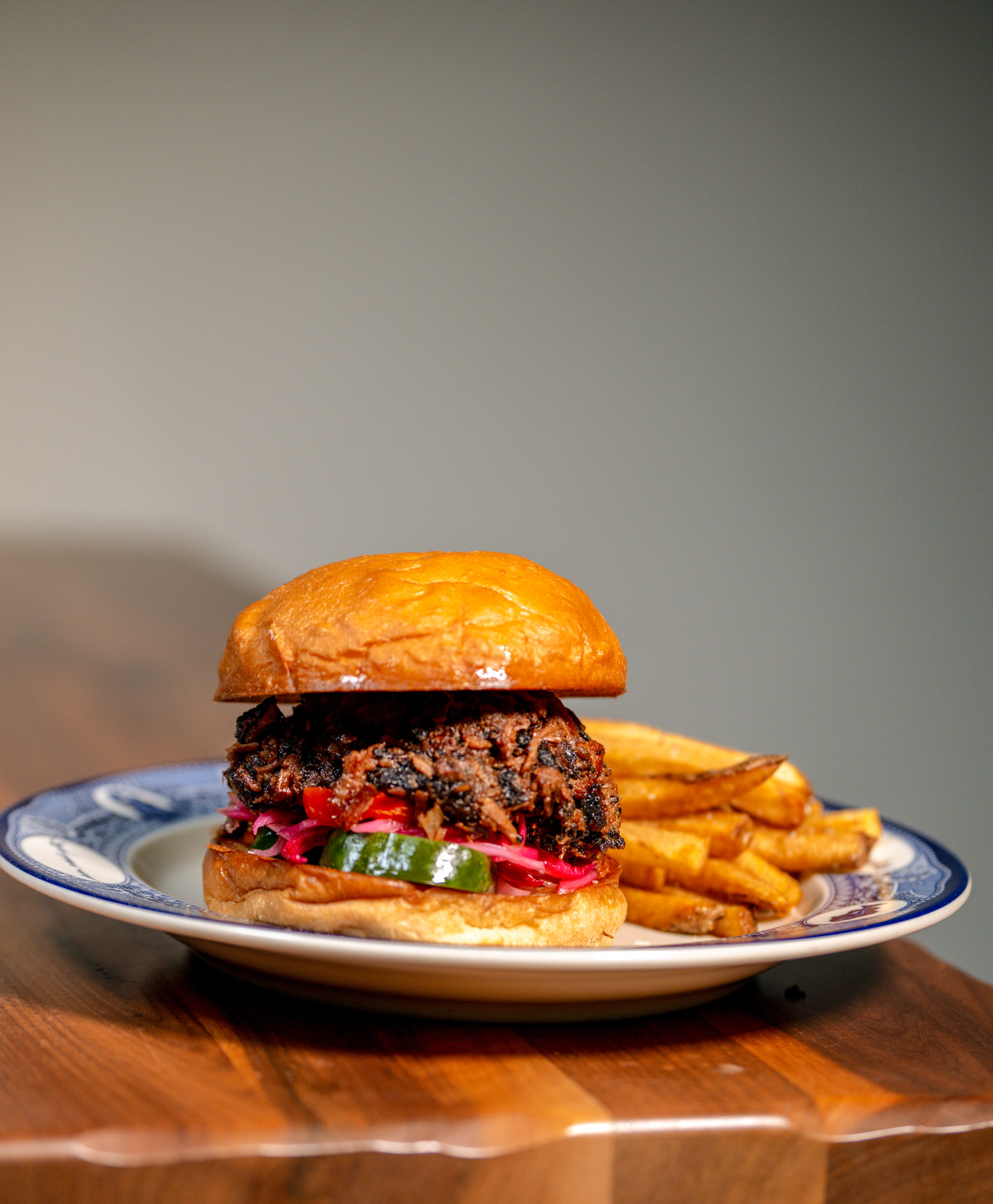 Texas BBQ Chopped Beef Sandwich on a toasted potato roll, piled high with chopped smoked beef, pickled red onions, bread and butter pickles, and pickled peppers, served with fries on a blue-rimmed Founding Farmers plate.