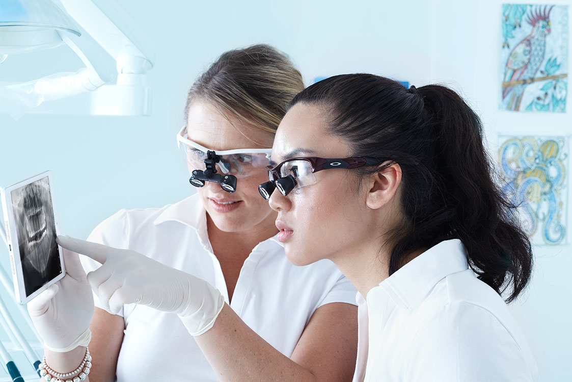 two women wearing loupes while reviewing x-ray