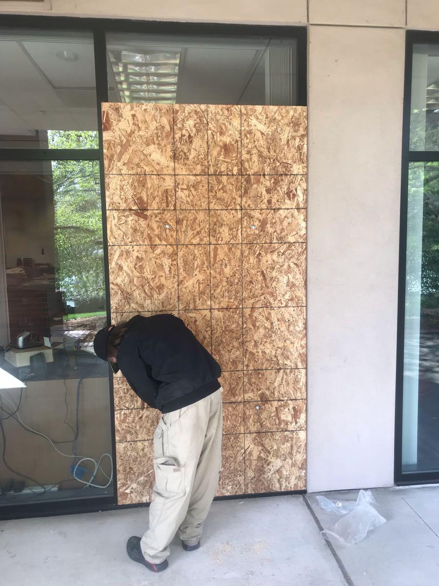 Tech in tan pants and black jacket boarding up an office building