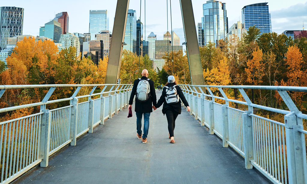 A couple walking hand in hand across a pedestrian bridge in Calgary.