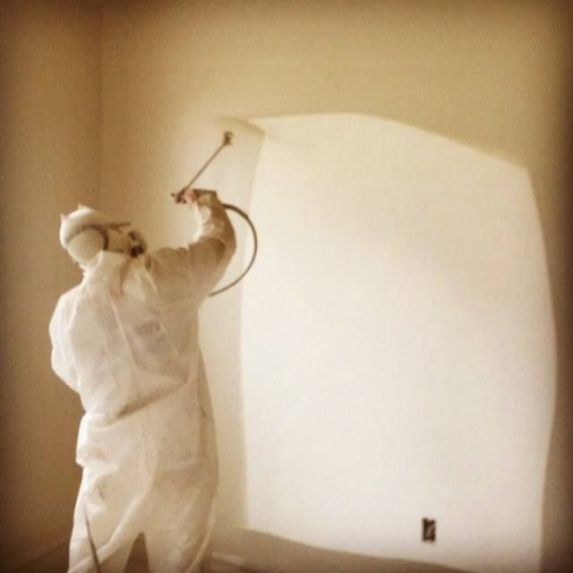 Painting contractor using spray equipment to apply smooth, even coatings on interior walls while wea 
