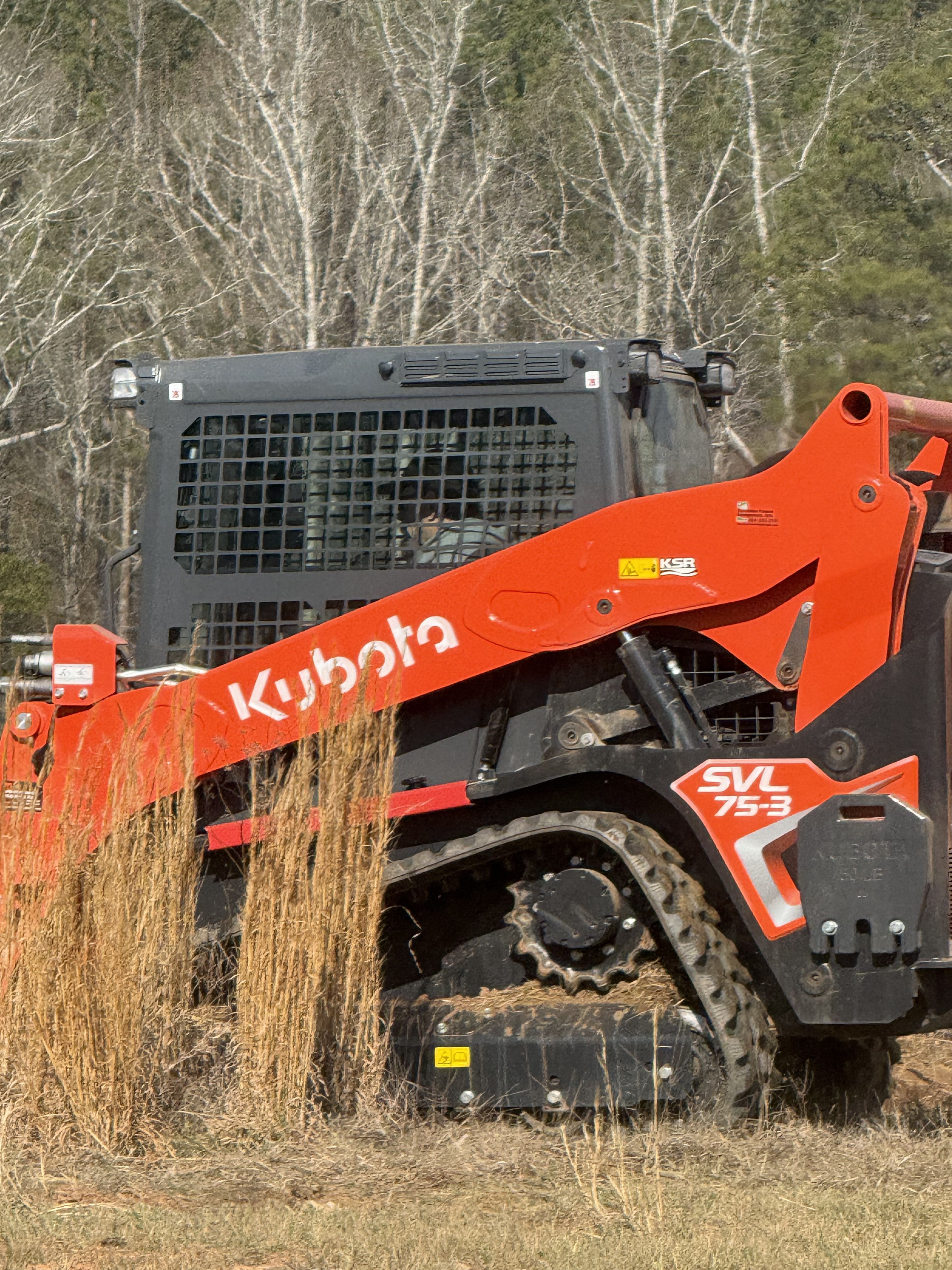 Photo of a Kubota track loader working near trees and brush for land clearing, forestry mulching, and property cleanup services.