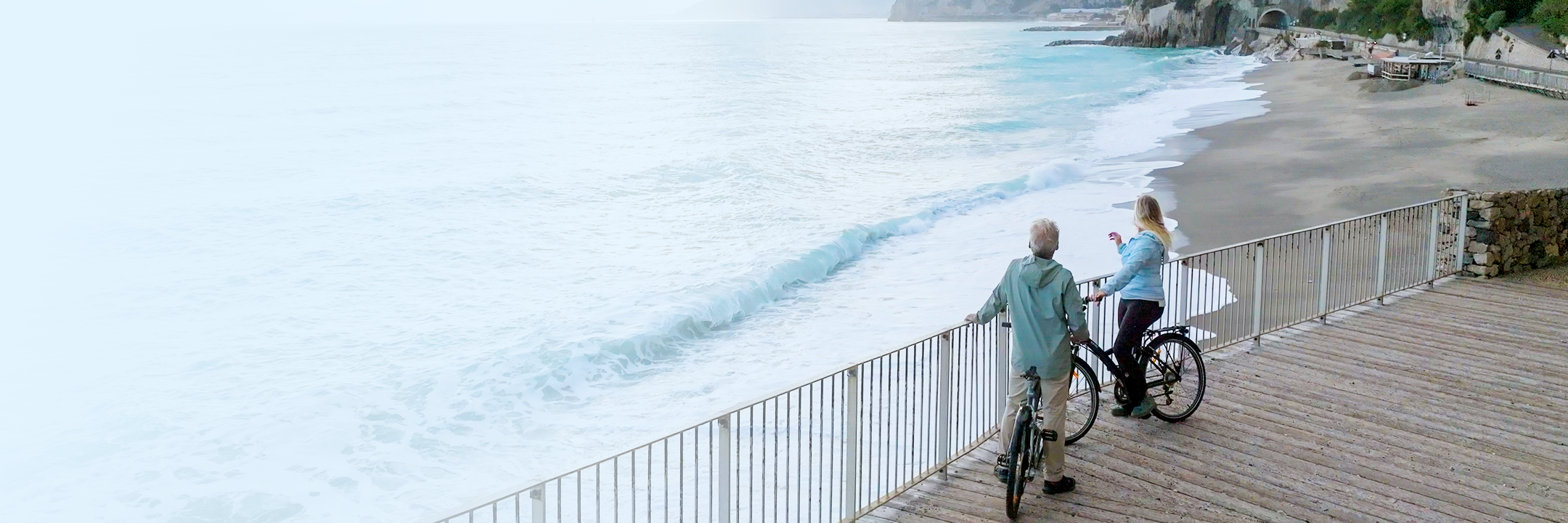A couple on a bike ride enjoying the view of the ocean from the boardwalk.