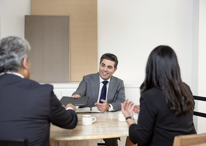 Maymar Naman handing a folder to two clients.