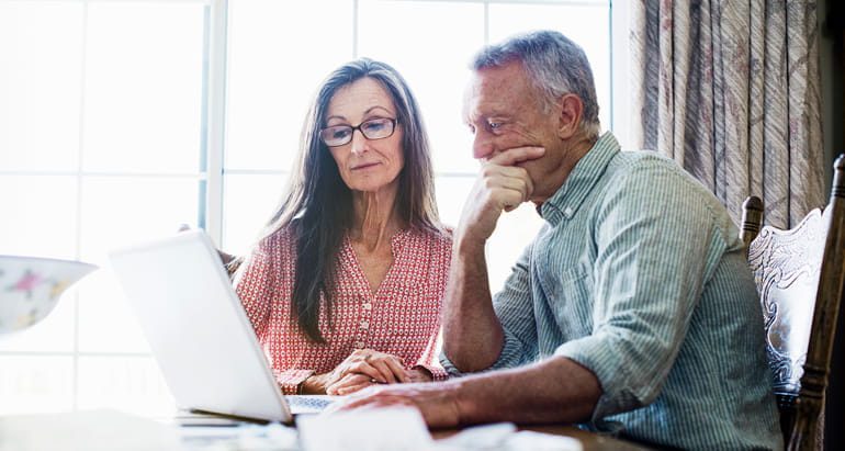A retirement aged man and woman review their financial accounts on a laptop computer.