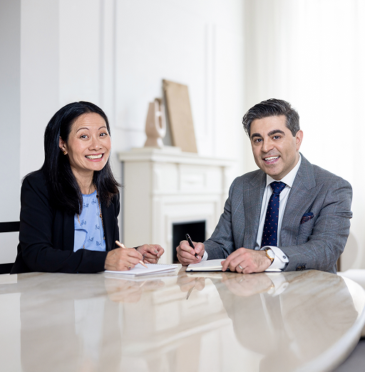 Maymar Naman and Jana Tom sitting together at a desk and smiling while writing in notebooks.