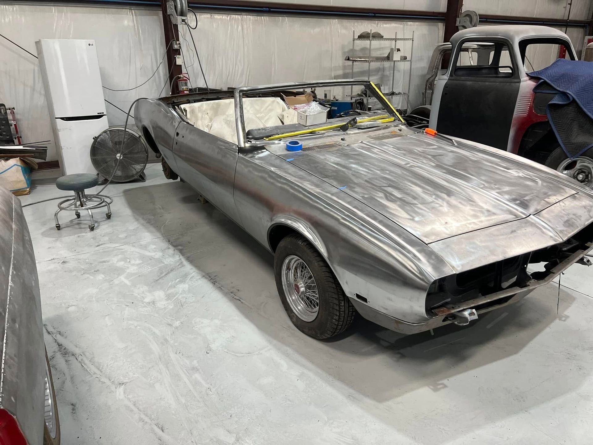 A classic convertible sits in a workshop during restoration. The body has been stripped and sanded, creating a clean surface ready for primer and refinishing work.
