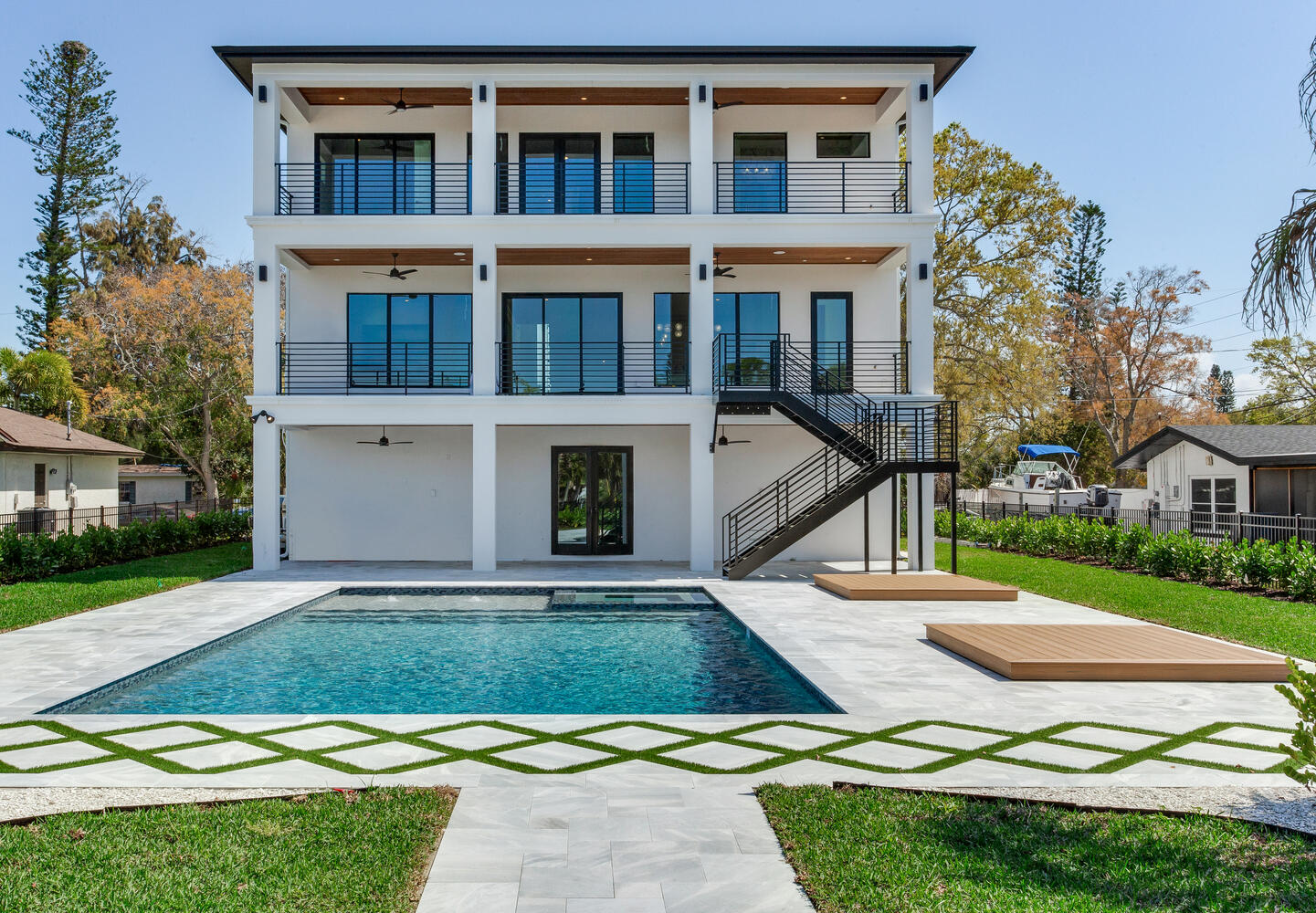 Modern elevated AVENTIS custom home exterior featuring multiple balconies, clean coastal architecture, manicured landscaping, and a spacious driveway.