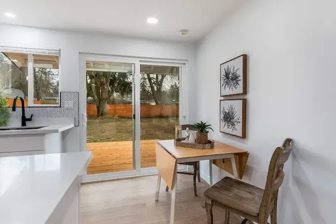 A modern kitchen and dining area features white cabinetry, bright countertops, a wooden dining table 