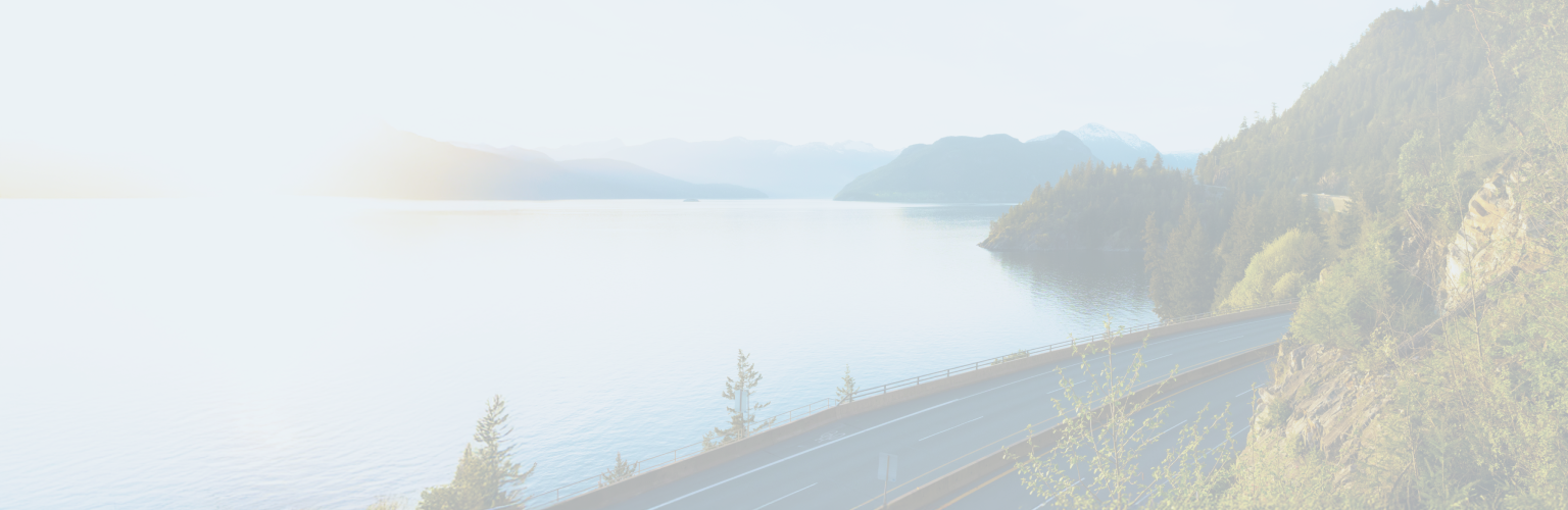 A road on a forested hillside that overlooks a lake and mountains in the distance.