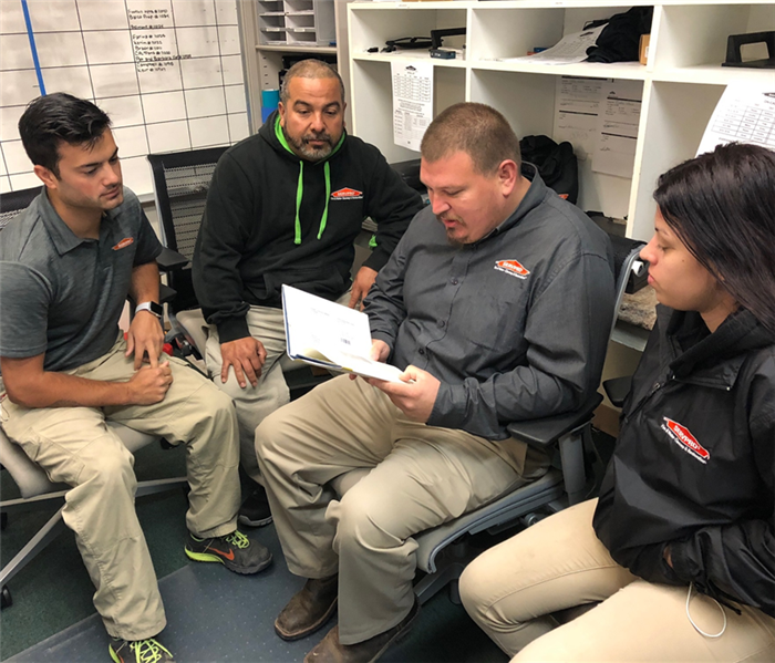 Jose Medrano, Production Manager (in center reading) is performing a training session with production department team members. Each week the managers at SERVPRO perform employee training and motivation using a book titled, The Four Disciplines of Execution. Our company calls this the 4DX Book. It teaches the managers and their team how to set goals, or to be more specific "Wildly Important Goals". Each week past goals are set and then reviewed for the success of their implementation. The former goals are adjusted, and or new goals are established for the following week. The idea is to be proactive. To always be moving forward. Instead of waiting until some project has been completed and then analyzing the final results, the 4DX program looks at indicators along the way.