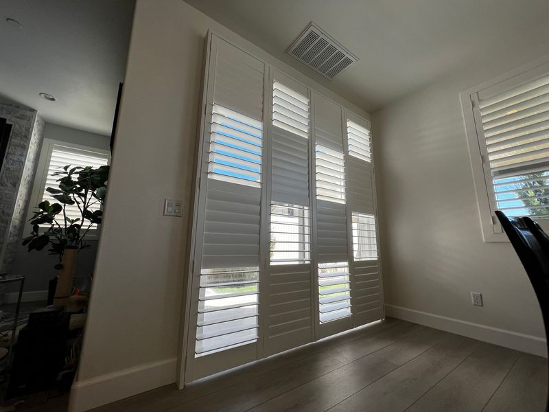 These elegant, full-height white shutters provide a custom solution for large glass doors. The split-louver design allows for simultaneous privacy and natural light, perfectly complementing the room&rsquo;s clean, contemporary aesthetic.
