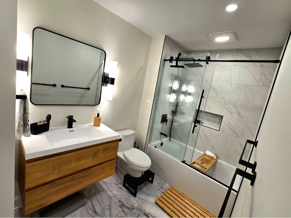 Remodeled bathroom featuring a wood vanity, bathtub, glass shower enclosure, and marble-look tile su 