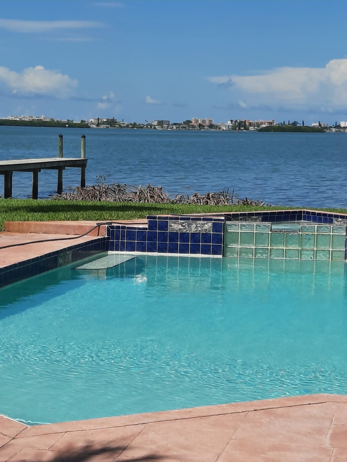 Waterfront residential swimming pool with turquoise water, decorative blue tile, and scenic views across the bay.