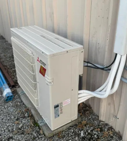 Outdoor Mitsubishi Electric mini split condenser installed beside a metal building, featuring insula 