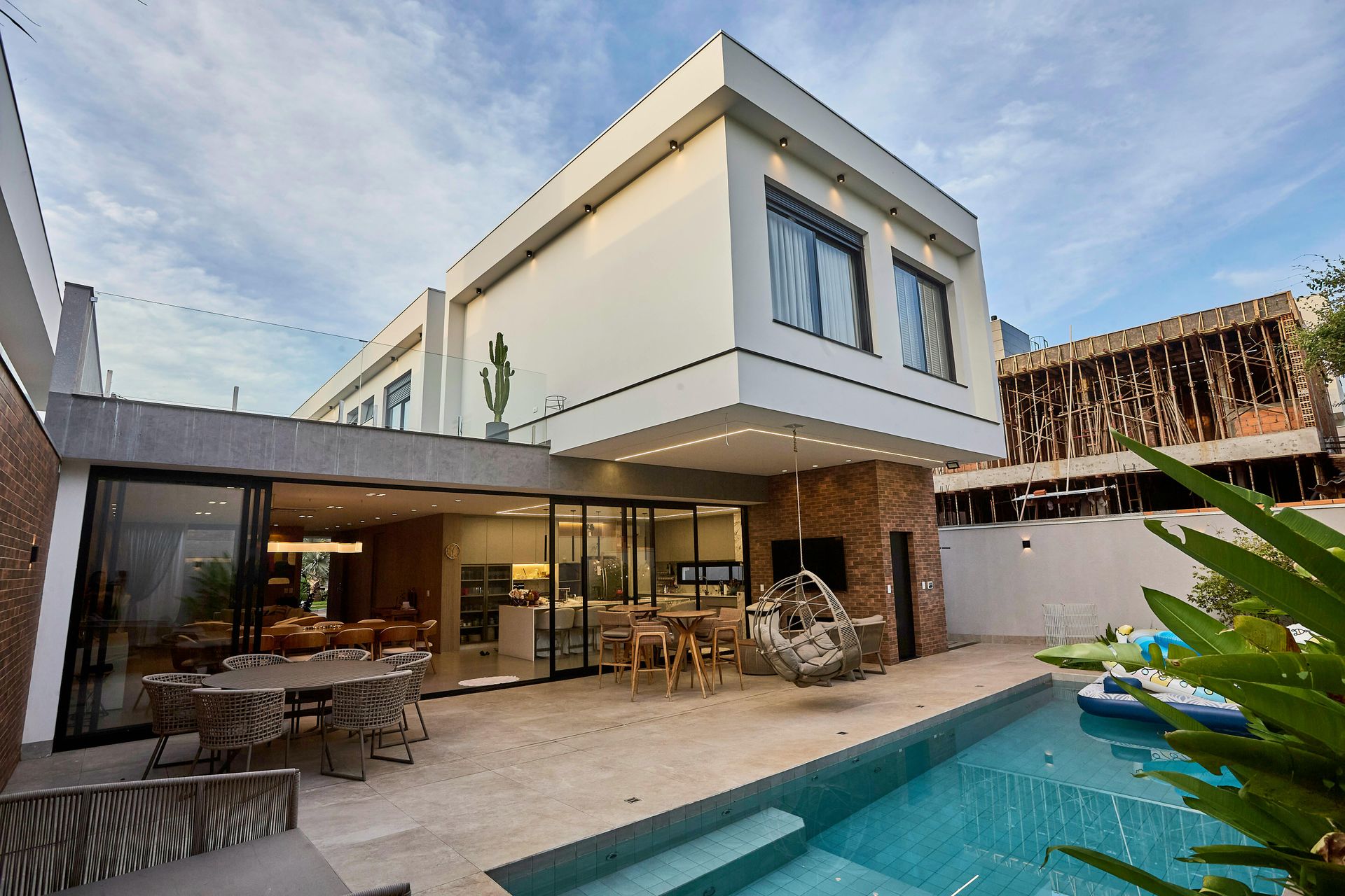 Contemporary luxury home with open layout, glass walls, outdoor seating, swimming pool, and modern architecture, showcasing high-end residential construction focused on indoor-outdoor living and elegant design.