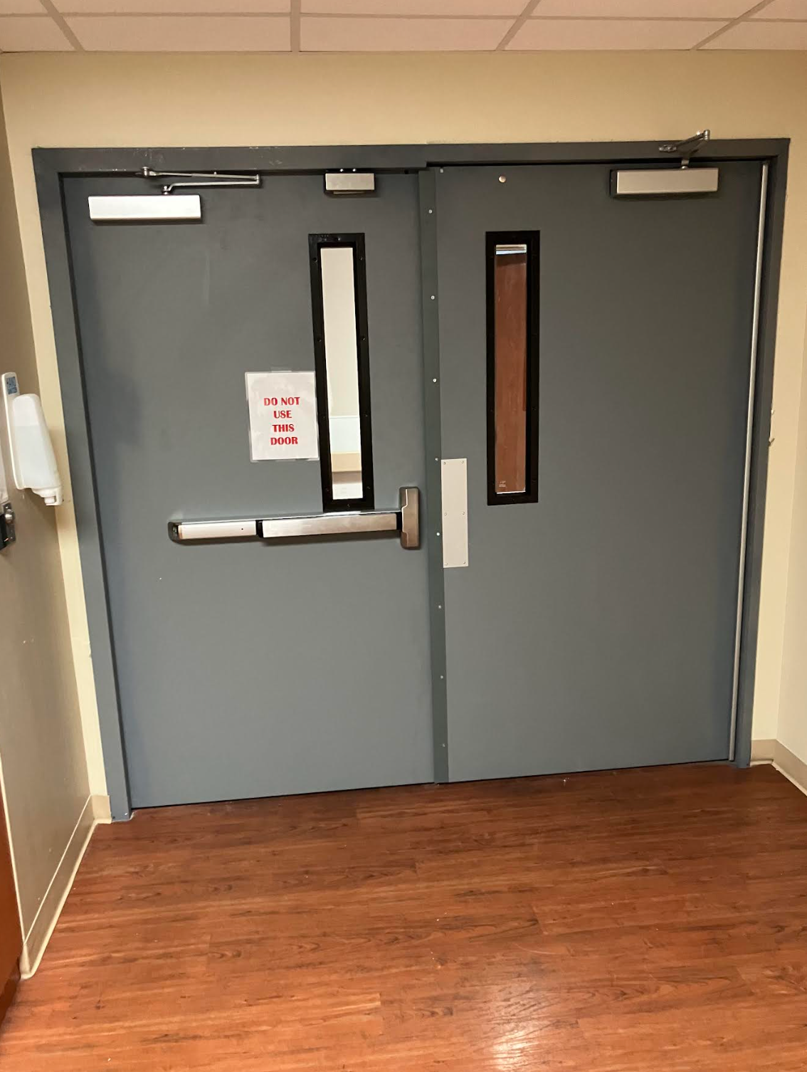 Gray commercial double doors with narrow windows, panic exit hardware, door closers, and durable construction installed inside a building hallway for safety and reliable daily use for commercial facilities daily.