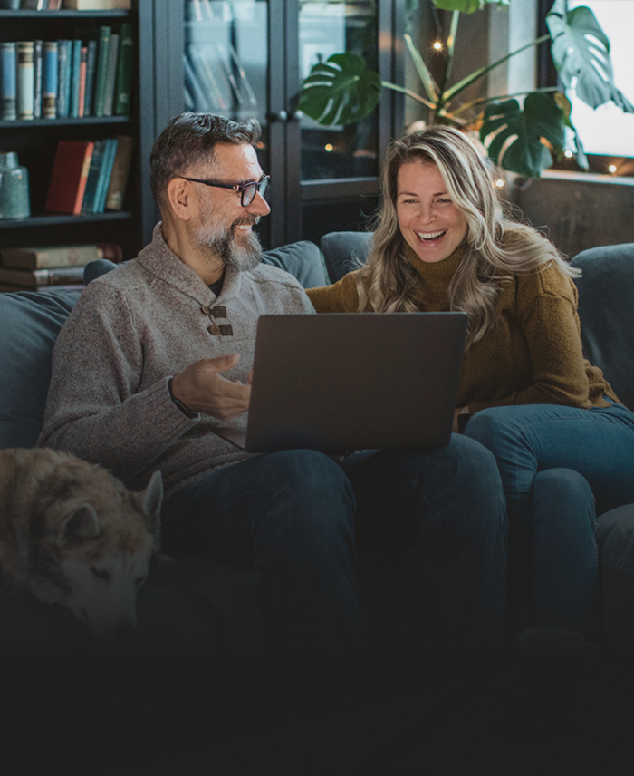 A couple on the couch laughing together while watching a show on their laptop.