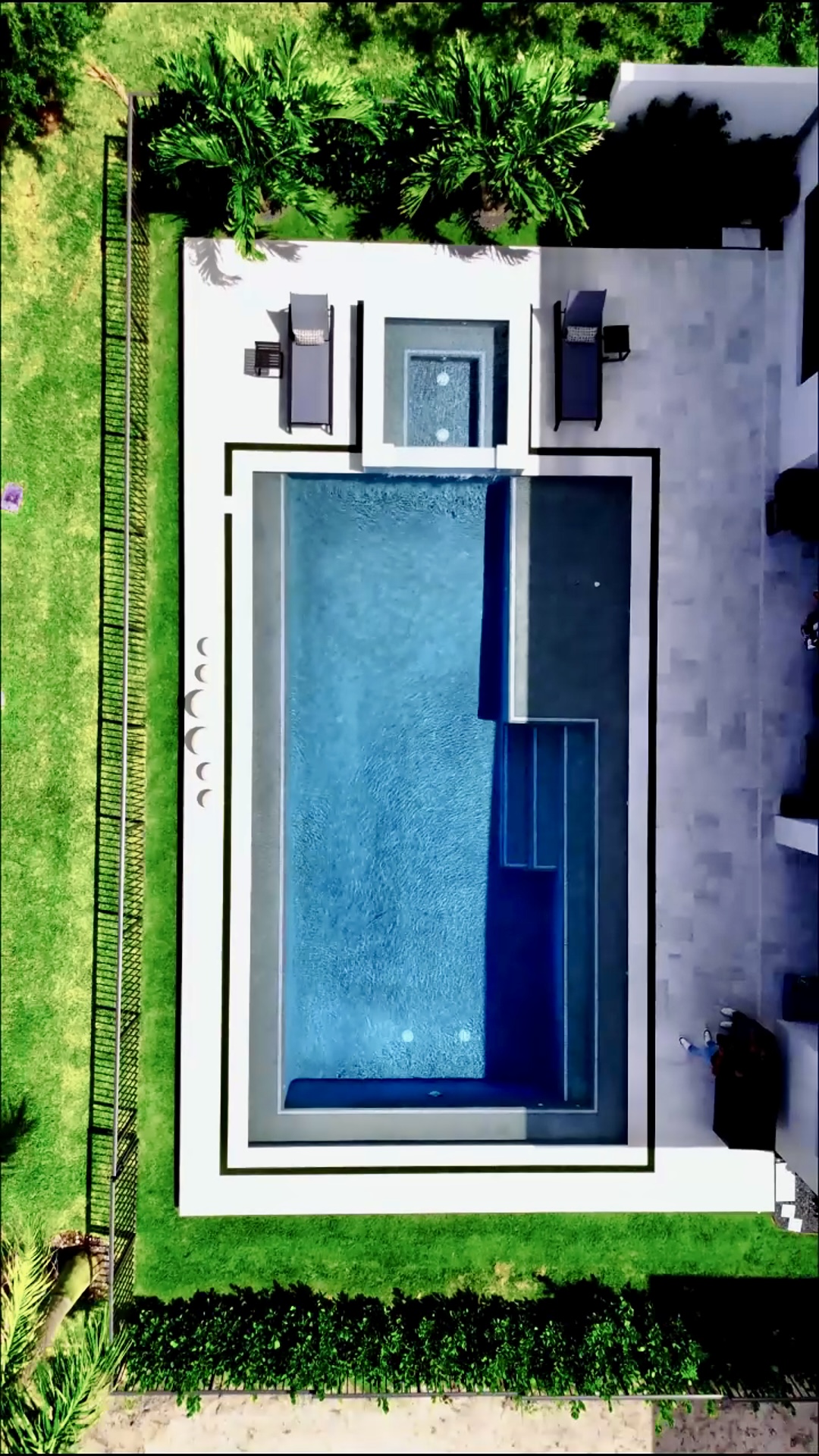 Aerial view of a sleek backyard pool with a raised spa, illuminated steps, and clean surrounding deck, showcasing modern pool architecture.