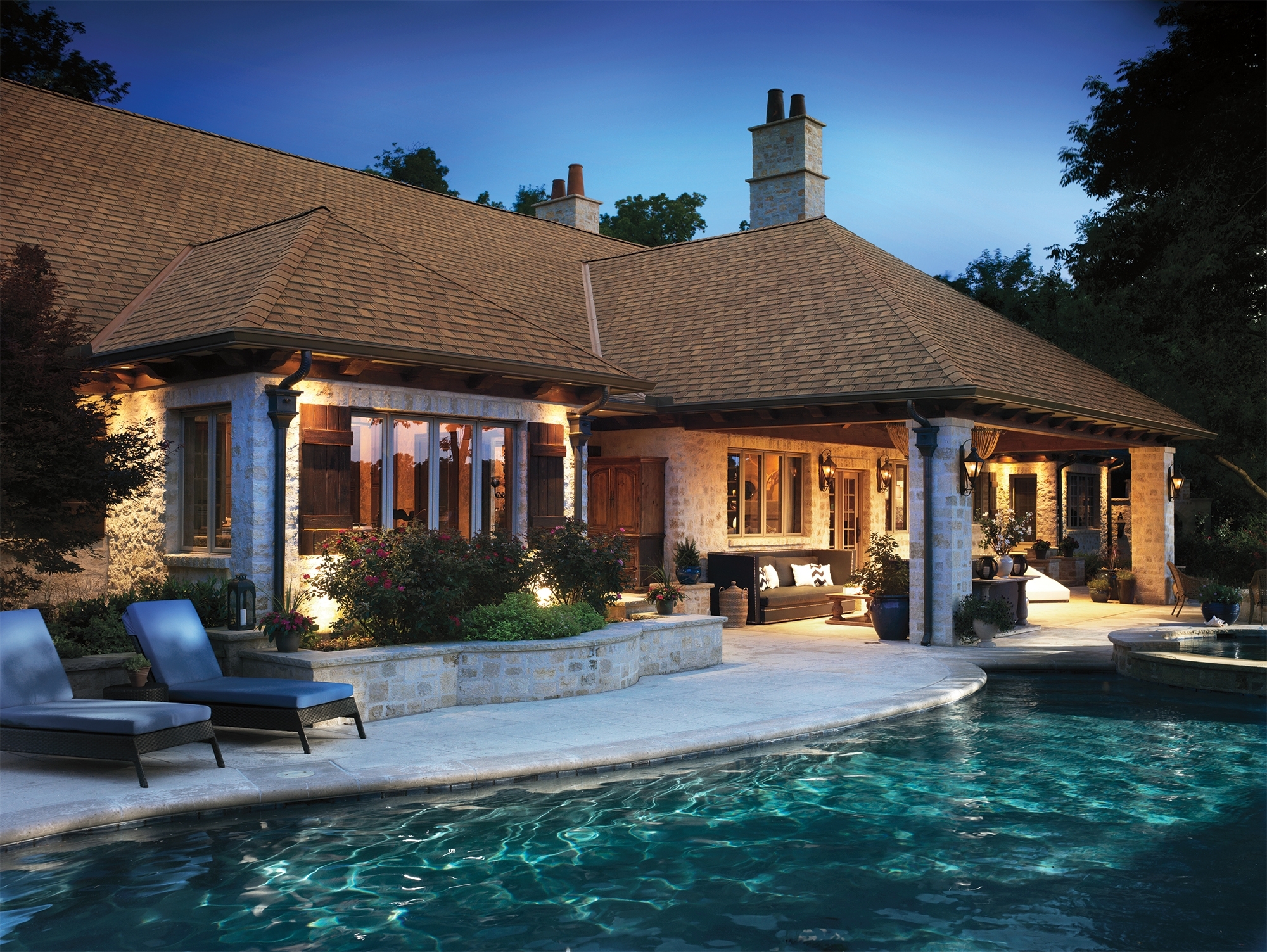 The GAF Timberline HDZ Camelot II roofing in Barkwood is showcased on a luxurious poolside home, providing an elegant and timeless aesthetic. The roofing's rich, deep tones perfectly complement the warm, earthy palette of the stone walls and wooden accents, enhancing the home's architectural beauty. Combining these high-quality shingles and natural elements creates a visually stunning and inviting outdoor living space.