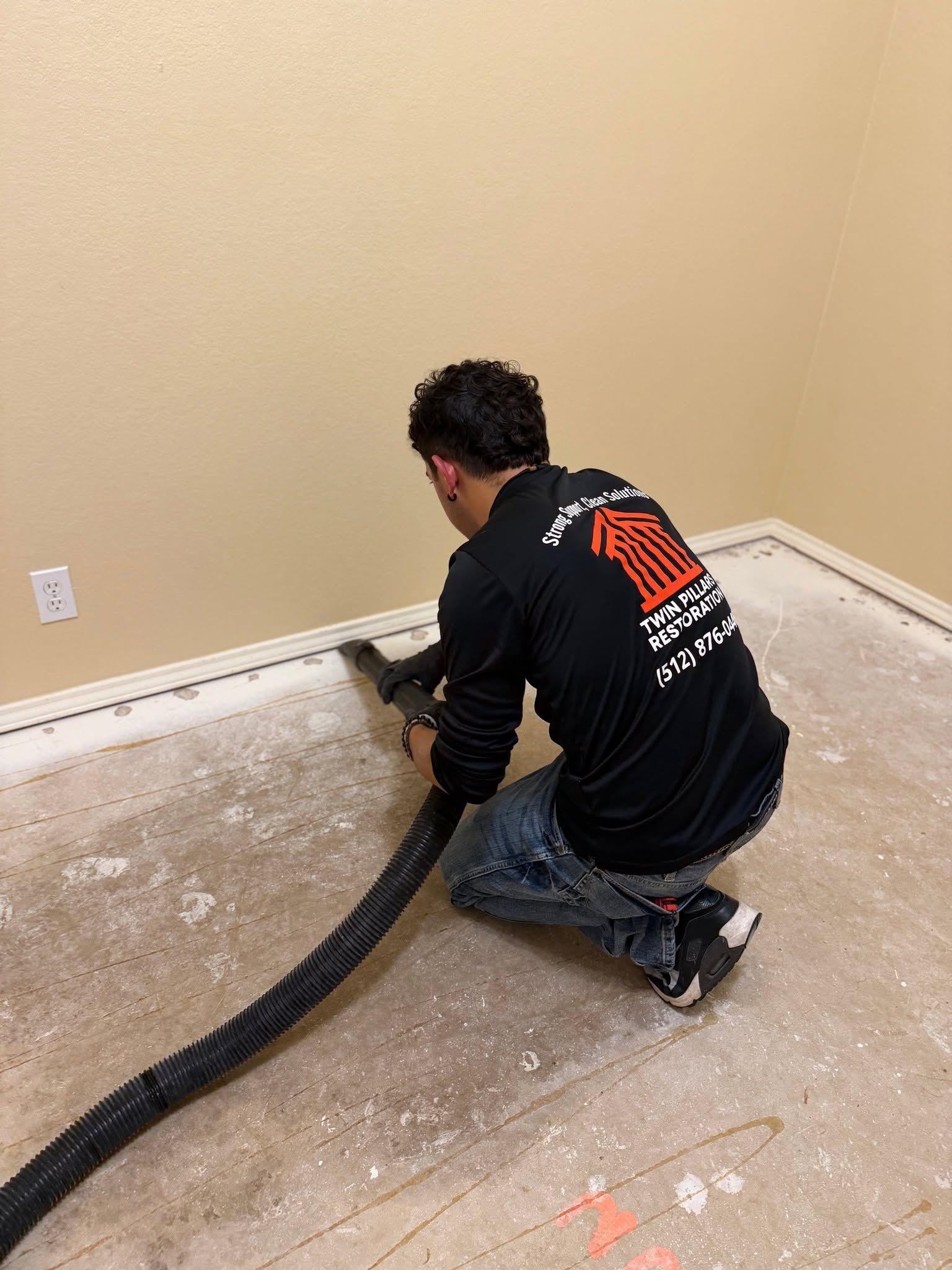A Twin Pillars Restoration worker kneels on a stripped interior floor while using a large extraction 