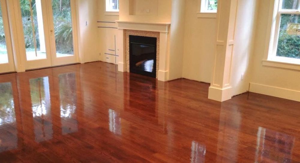 Spacious living room with polished hardwood floors, white walls, large windows, and fireplace, reflecting natural light and showcasing clean, elegant interior design ideal for residential home improvement.
