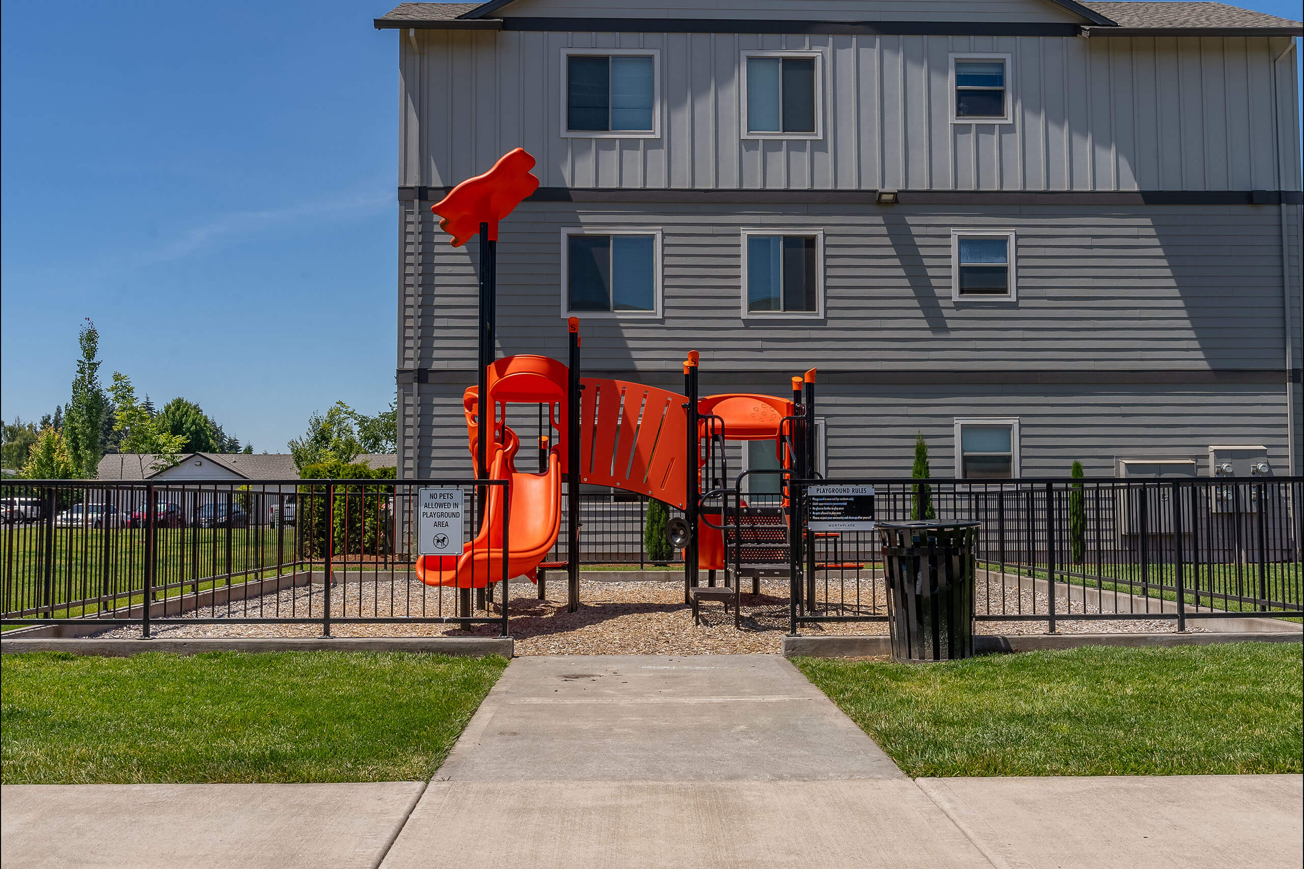 A playground with a red slide in front of a grey building.